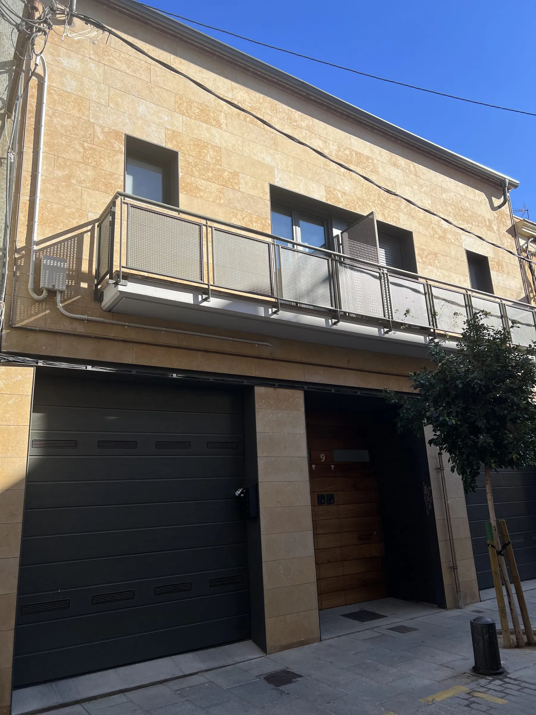 Casa pareada terminada en Cornellà de Llobregat, con fachada de piedra clara, balcón corrido y puertas de garaje oscuras